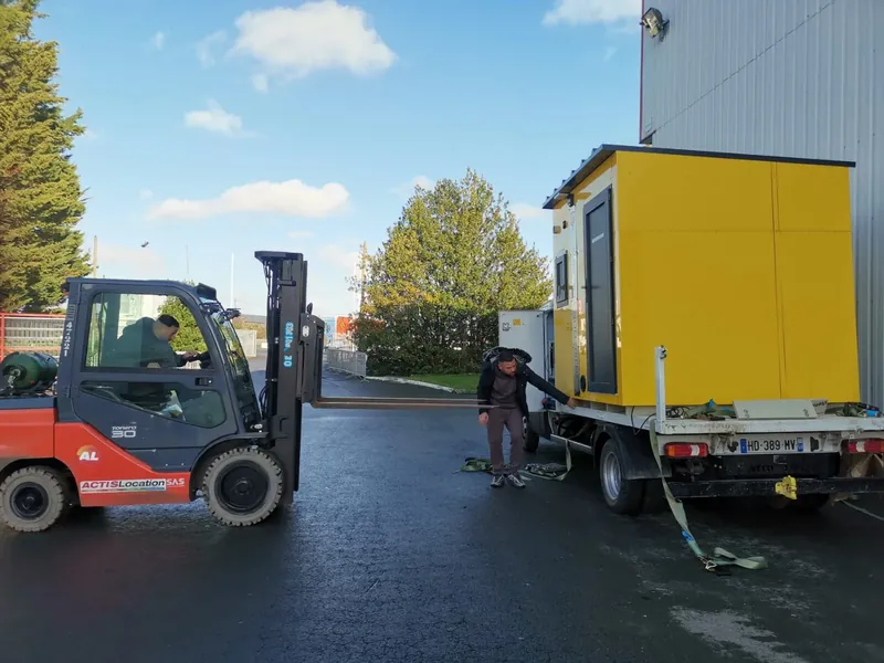 Station ITB Outdoor à bardage jaune déchargée d’un camion plateau à l’aide d’un chariot élévateur